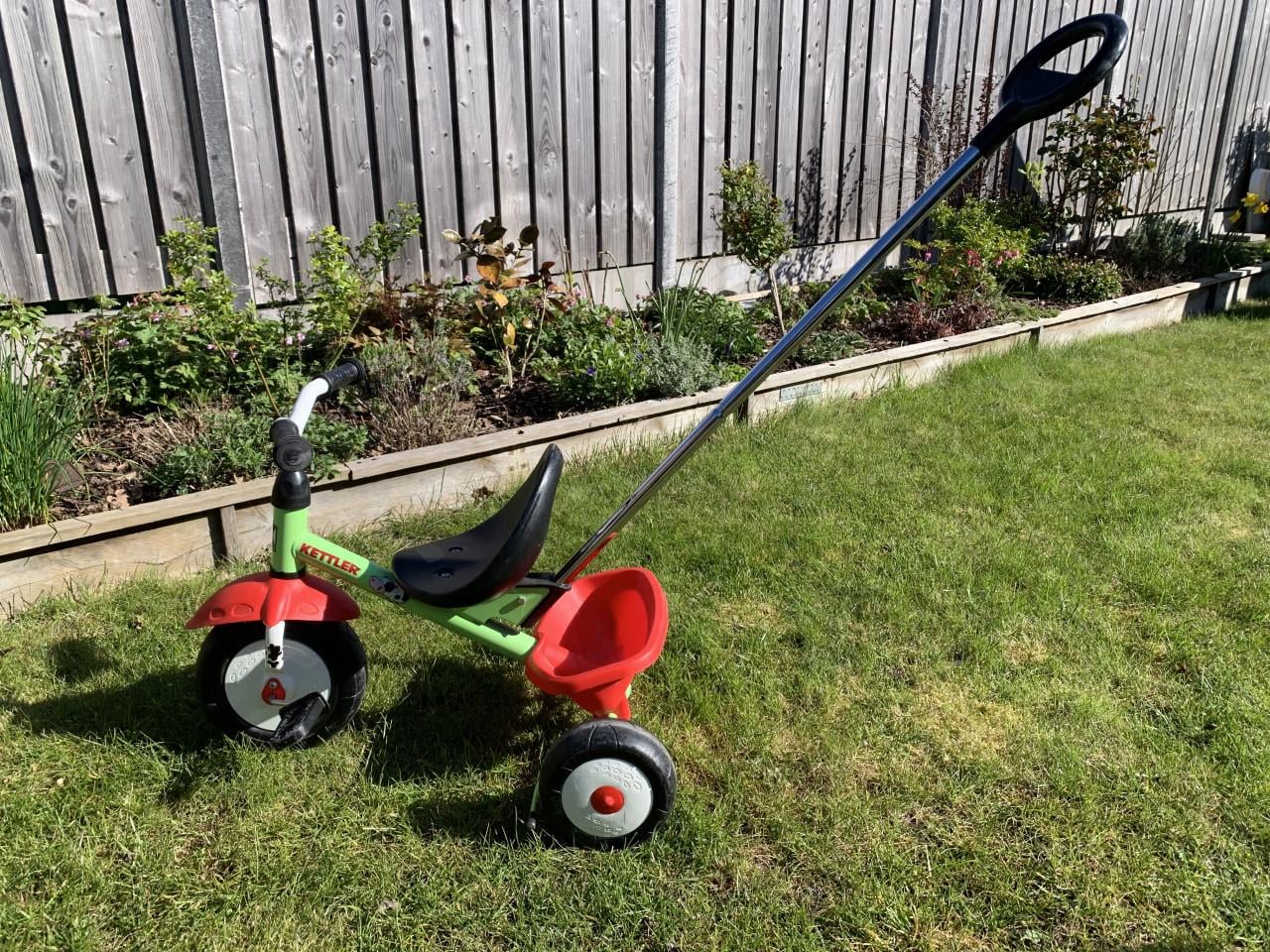 Een groene Kettler driewieler met duwstang