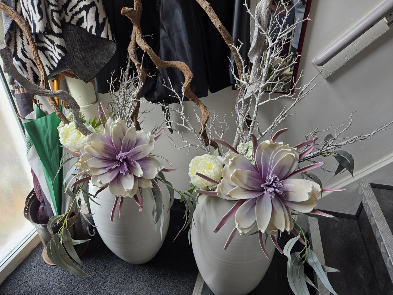 2 grote, witte vazen gevuld met decoratieve kunsttakken en kunstbloemen