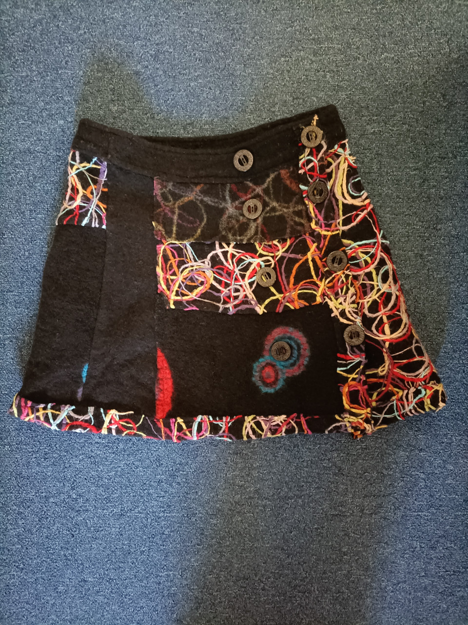 Rok gekleurd, ondergrond zwart. Leuk met knopen. Maat S 36/38.