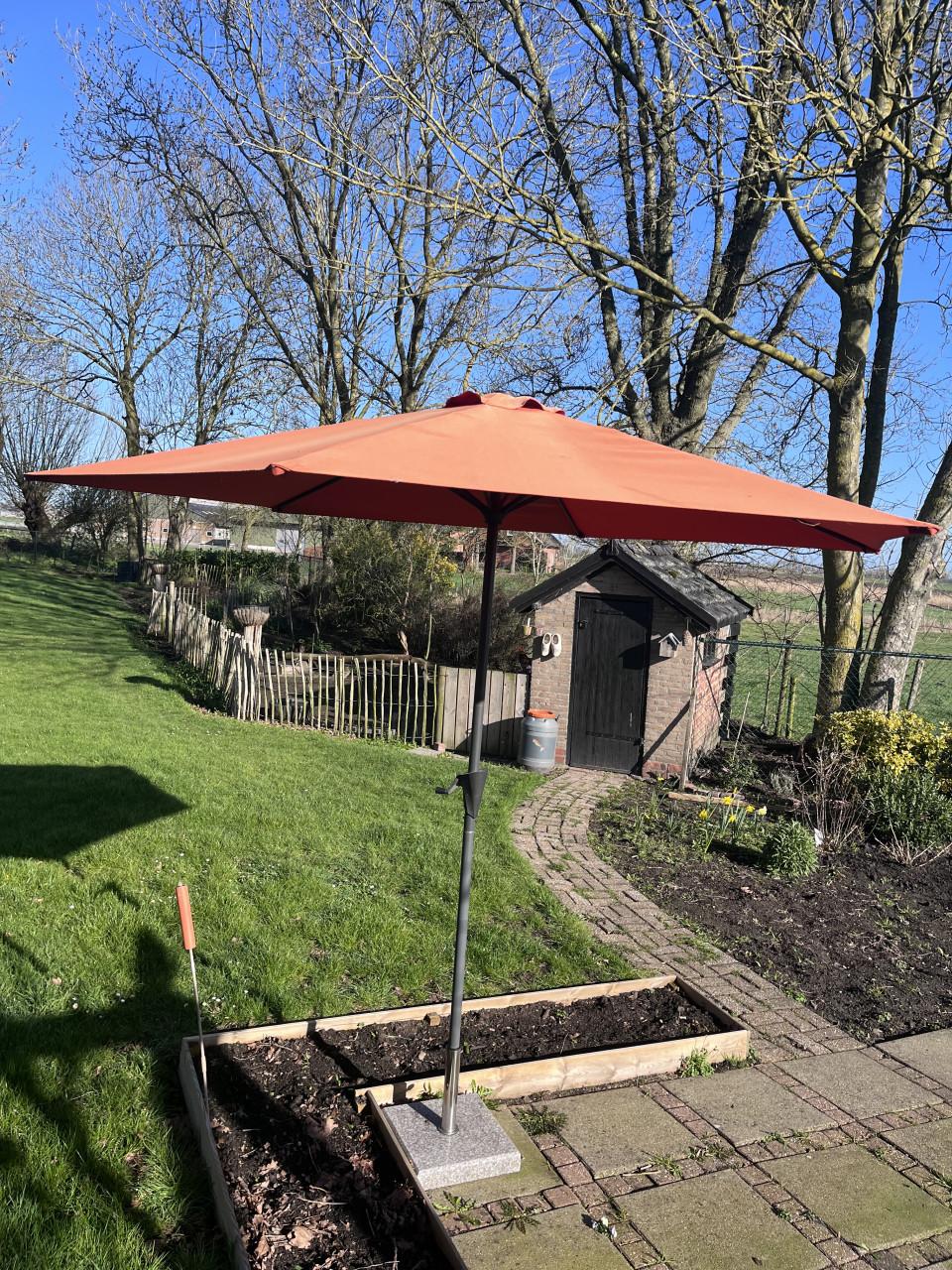 Oranje parasol met voet van steen
