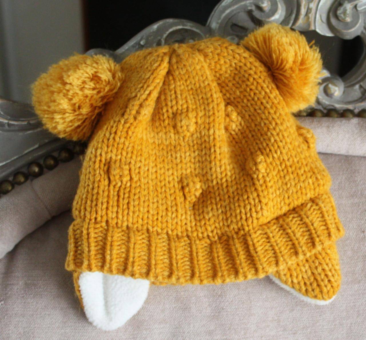 Oker gele babymuts met bollen en oorflappen maat 0-4maanden