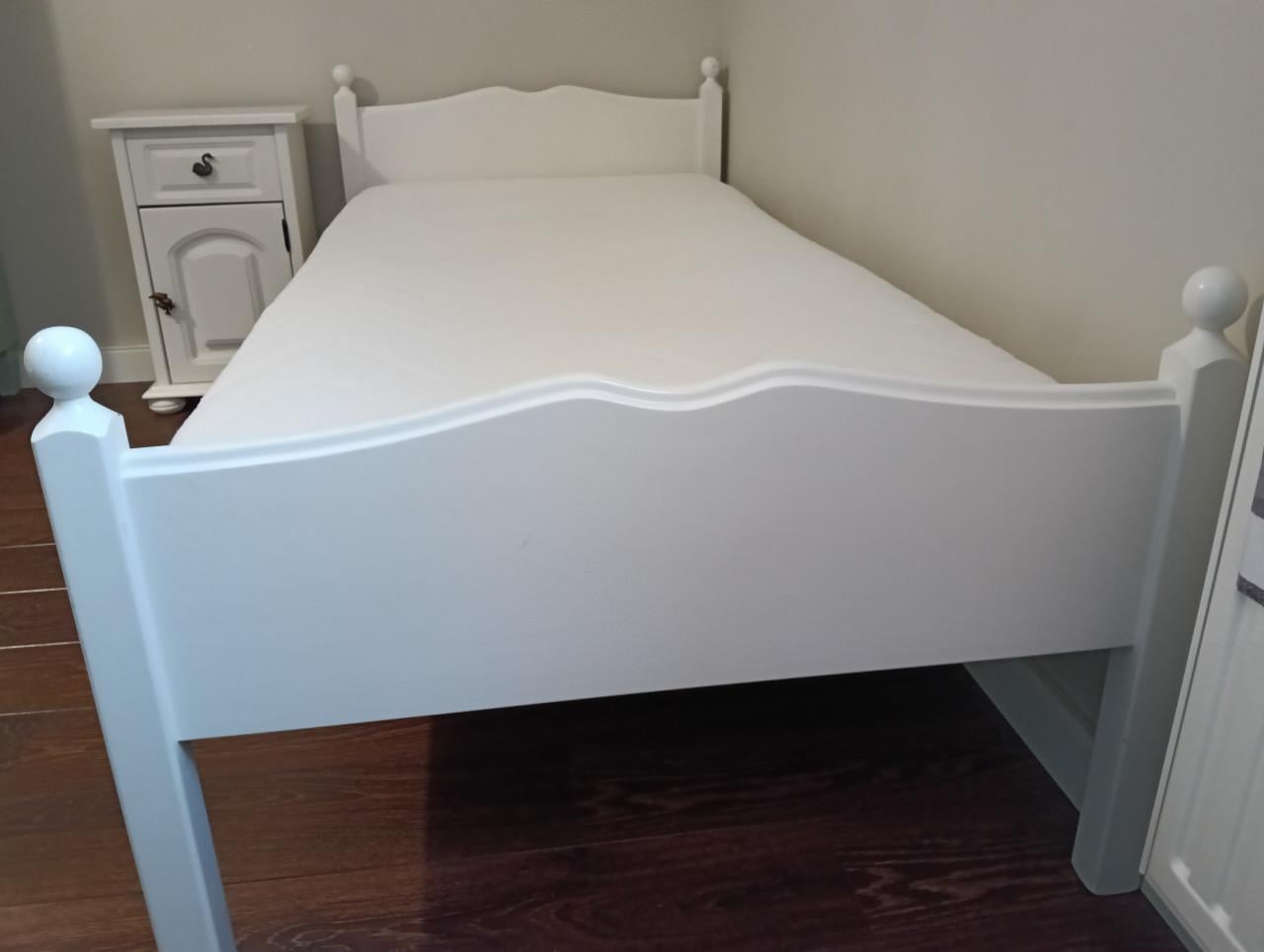 Wit eenpersoons bed met lattenbodem en nachtkastje.