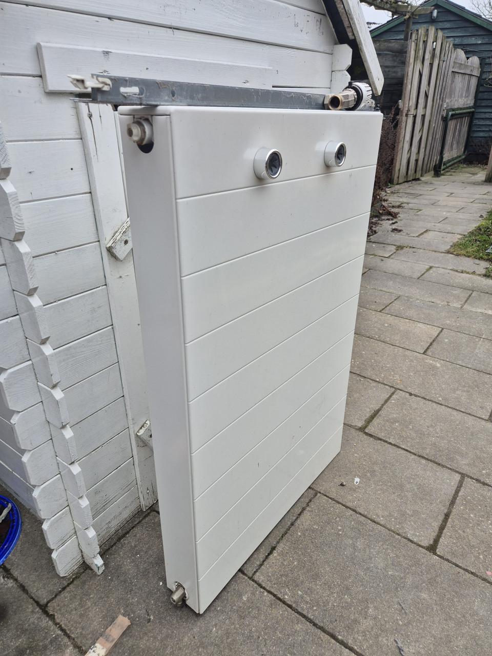 Nette radiator met ophangsysteem en thermostaatknop.