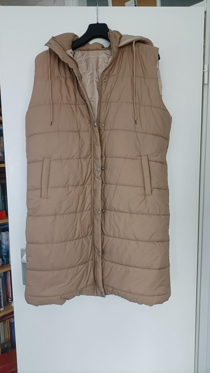 Lange dikke bodywarmer met capuchon. Lichtbruin van kleur. Maat 44/46. Slui