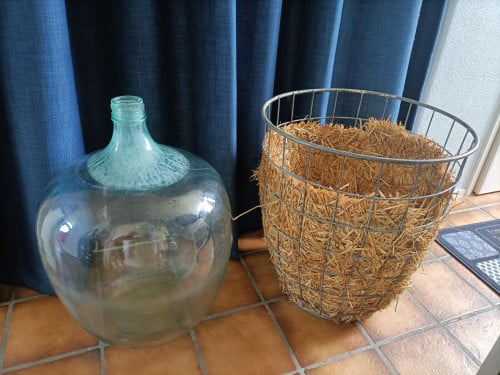 Brocante grote gistfles of wijnfles in ijzeren mand/korf.