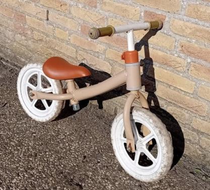 Een loopfiets in beige kleur met een bruin zadel