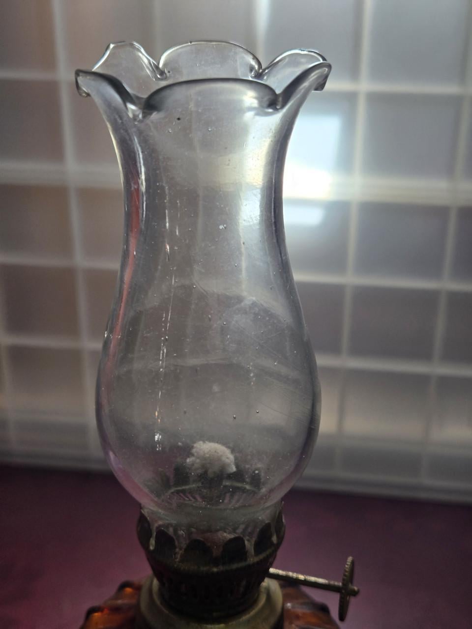 Vintage olielamp met een amberkleurige glazen voet en glazen cilinder.