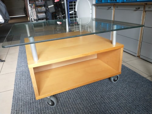 Salontafel, licht hout met hardglas en zwenkwielen.
