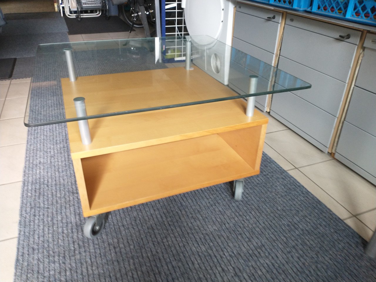 Salontafel, licht hout met hardglas en zwenkwielen.