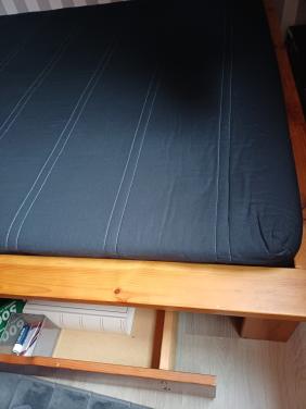 Bed met matras plus lang hoofdkussen en bedlade onder het bed.