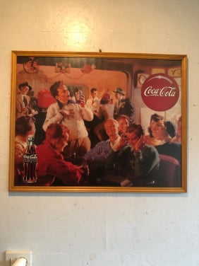 Coca cola poster ingelijst achter ontspiegeld.