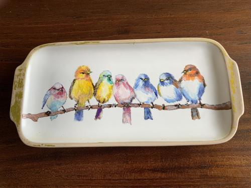 Een rechthoekige schaal met zeven gekleurde vogels op een tak