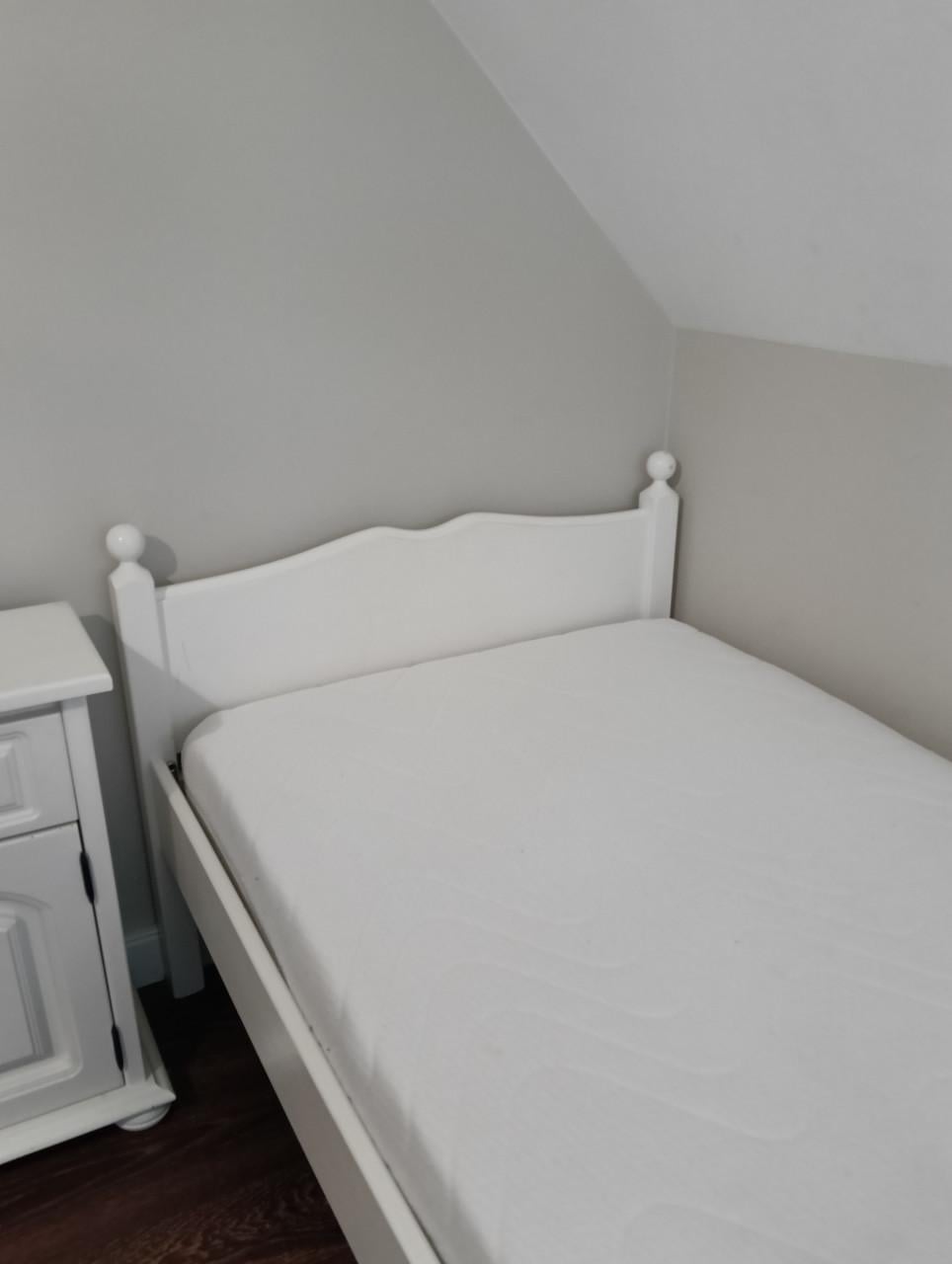 Wit eenpersoons bed met lattenbodem en nachtkastje.